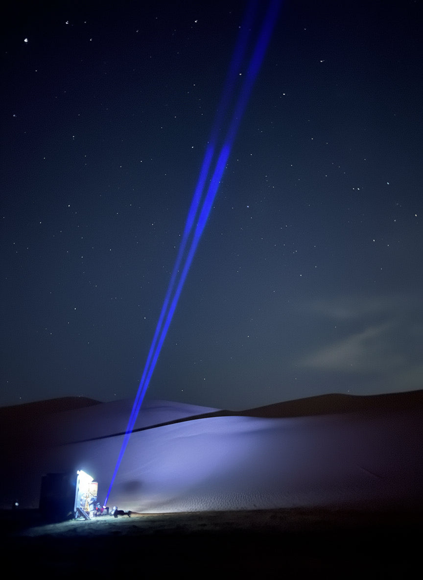 Blue laser pointer beam against a night sky with trees