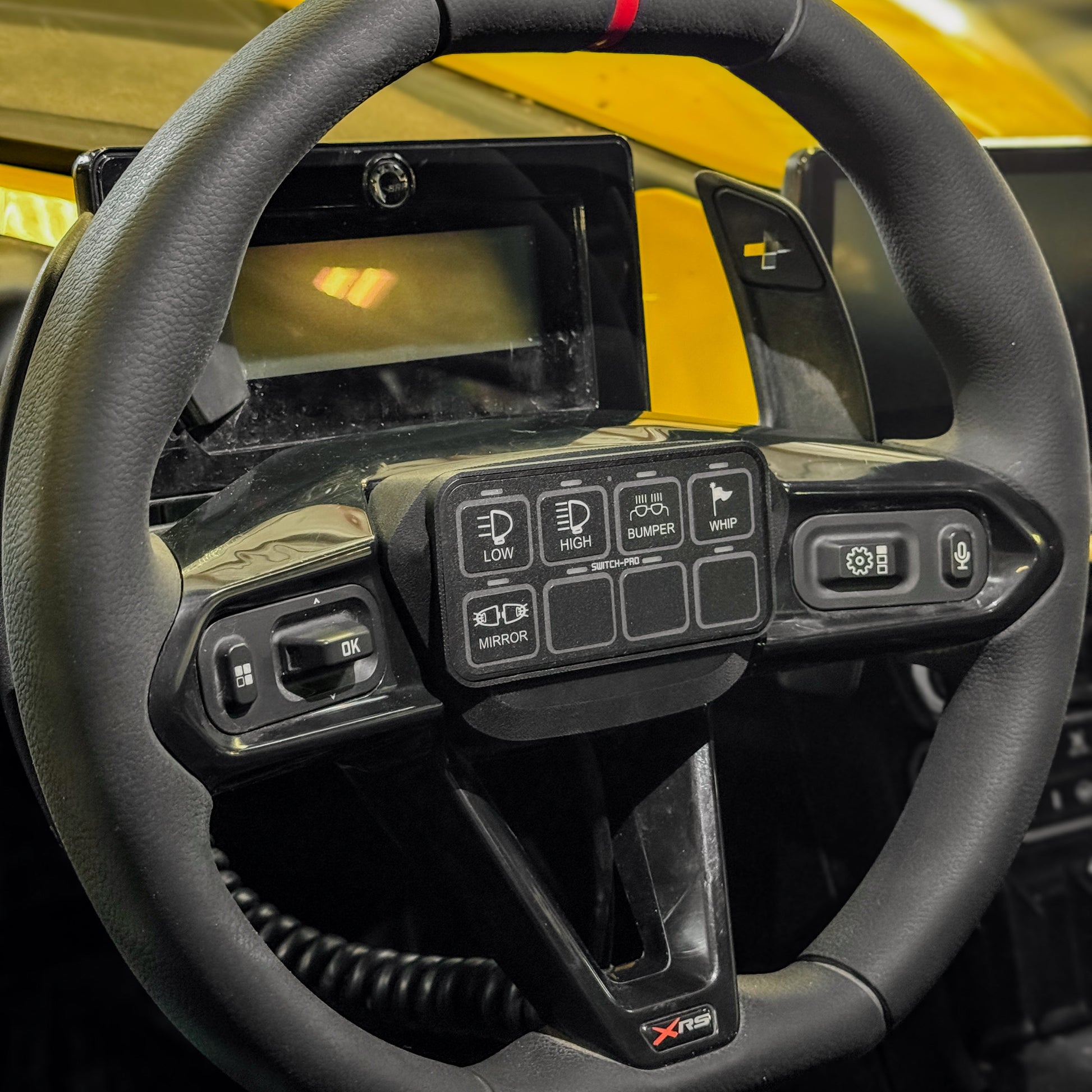 MTS Offroad Switch Mounted mounted on a car black steering wheel with yellow paint in the background